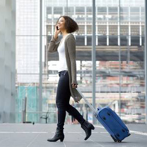 A woman walking through an airport with a suitcase and phone in hand.