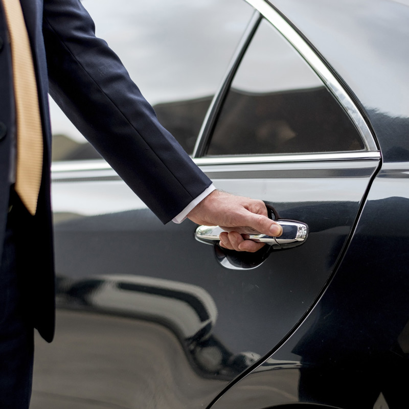 A man in a suit opening the door of a black car.